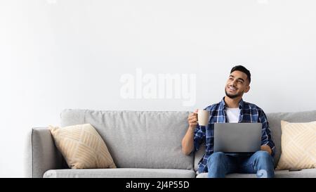 Man using pc sitting on the couch, drinking coffee Stock Photo