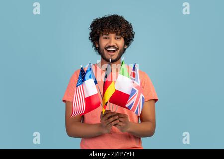 Happy hindu guy holding diverse flags, blue studio background Stock Photo