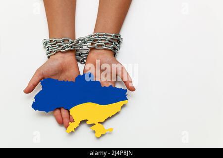 Women's hands are tied with a chain and holding a map of Ukraine painted in blue and yellow on a white background. Take away freedom and independence. Stock Photo