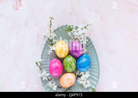 Colorful Easter eggs on plate and spring white cherry blossom flowers on pink background. Easter celebration concept. Top view, flat lay, copy space Stock Photo