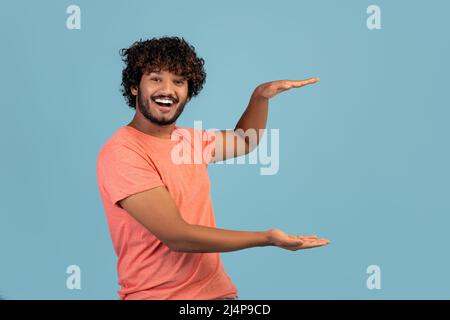 Cheerful positive indian guy showing something invisible Stock Photo