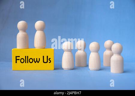 Follow us text on yellow wooden block surrounded by wooden dolls. Stock Photo