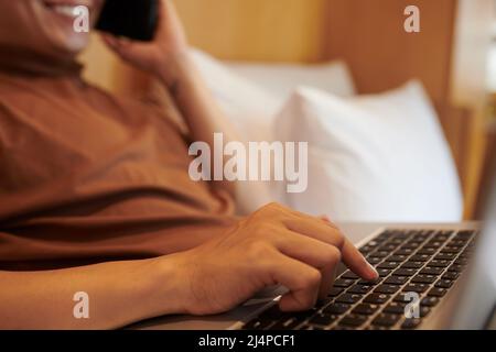 Young man pushing button on laptop when talking on phone with colleague or client Stock Photo