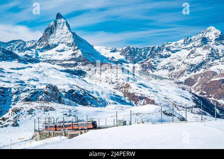 Red train climbing up to gornergrat station with view of Matterhorn against sky Stock Photo