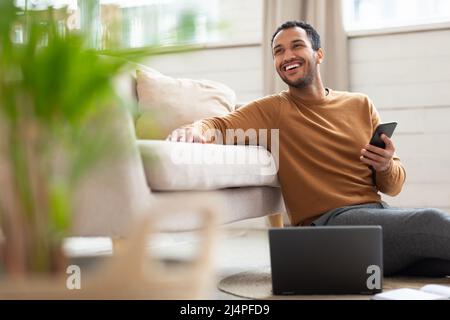Young Arab man holding phone using pc at home Stock Photo