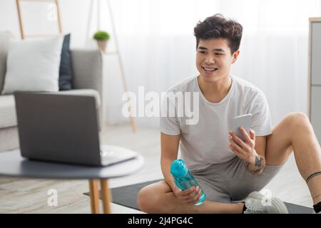 Asian guy doing exercises at home watching online tutorial Stock Photo