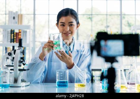 Portrait of young female doctor wearing lab coat recording online video class and vlog on medical research and science experiments in laboratory Stock Photo