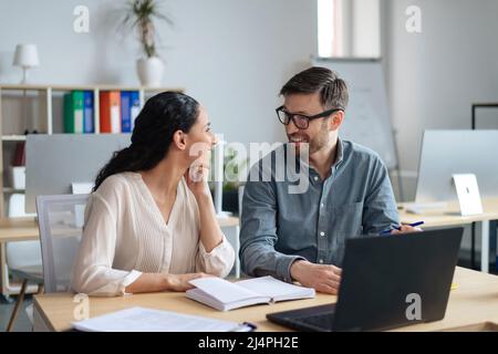Teamwork and collaboration concept. Happy young coworkers having friendly communication at workplace Stock Photo