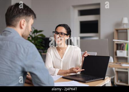 Happy millennial colleagues working together on online business project, using computer with mockup at office Stock Photo