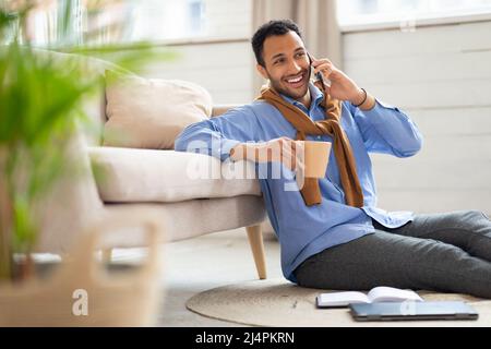 Smiling man talking on phone at home, drinking coffee Stock Photo