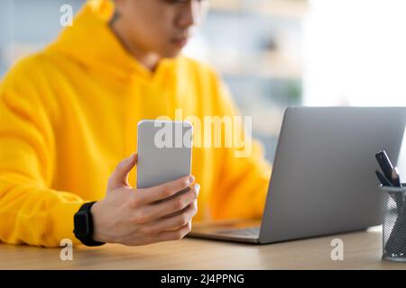 Asian man sitting at desk using cell phone, closeup Stock Photo
