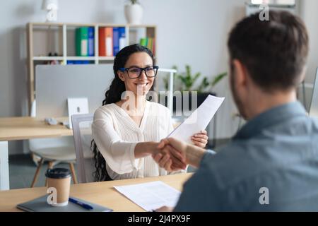 Smiling female personnel manager and job applicant shaking hands after successful employment interview at office Stock Photo