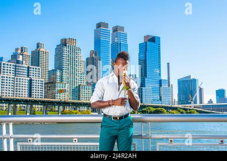 Missing You. Wearing a white, long sleeve shirt,  green pants, a young black guy with mohawk hair is standing in the front of buildings, hands holding Stock Photo