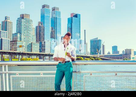 Waiting for You. Wearing a white, long sleeve shirt,  green pants, a young black guy with mohawk hair is standing in the front of buildings, hands hol Stock Photo