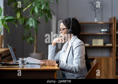 Young positive african woman remote recruiter using wireless headset to communicate with candidates Stock Photo