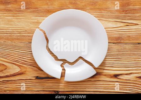 Top view on broken circle white plate on wooden background. The plate broke into three pieces. Stock Photo