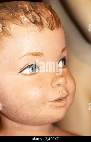Closeup of face of cracked vintage little boy mannequin with foreground painted eye in focus Stock Photo