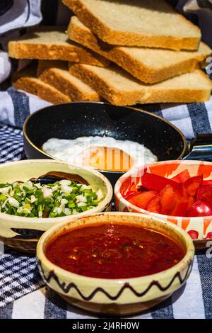 Close up of fried egg in a small frying pan  and different bowls with copped vegetables in a rustic composition Stock Photo