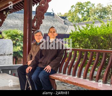 Senior Man and Woman sitting on a long bench to take a break. A  senior couple, 80 years old, is sitting on a bench inside a buddhist temple while vis Stock Photo