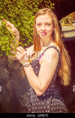 Beautiful American teenage girl with long blonde hair happily looking at green leaves at Central Park, New York, in sunny spring day. Instagram Filter Stock Photo