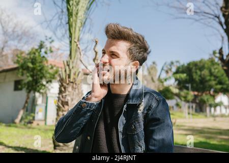 Toothache, young man holding his chin in front of aching tooth, a young adult with a fear of the dentist Stock Photo
