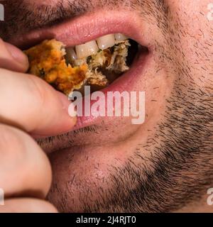 Detail of man taking a bite of freshly fried meatballs Stock Photo