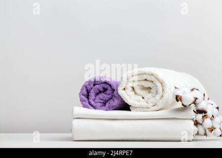 White bed linen, sheets and terry towels with a cotton branch on a light gray table Stock Photo