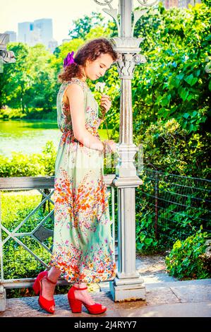 Lady Missing You at Park. Dressing in sleeveless, light green, long dress, red sandals shoes, pretty teenage girl standing inside pavilion, hand holdi Stock Photo