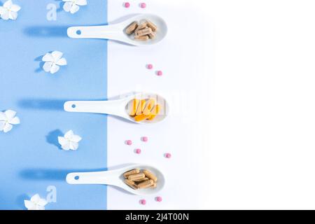 Flat lay composition of three white spoons with nutritional complexes on white and blue background with copy space. Foodstuffs concept. Stock Photo