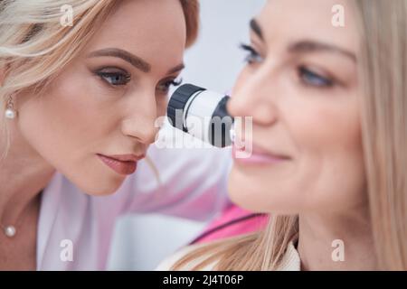 Concentrated middle-aged lady doctor performing dermoscopy procedure Stock Photo