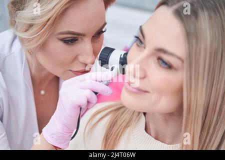 Experienced Caucasian female dermatologist performing dermatoscopy procedure Stock Photo