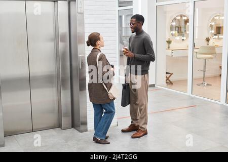 Waist up portrait of two young coworkers chatting while standing by elevator in modern office building Stock Photo