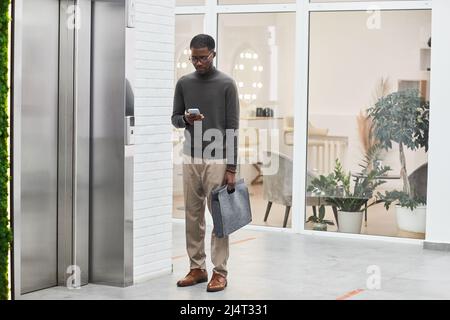 Minimal full length portrait of young black businessman standing by elevator in modern office building, copy space Stock Photo