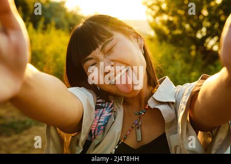Asian young woman showing her tongue while taking selfie photo outdoors Stock Photo