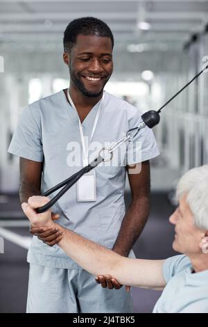 Vertical portrait of smiling rehabilitation therapist assisting senior man at gym in clinic Stock Photo