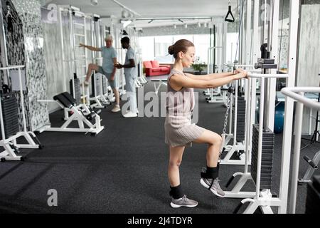 Side view portrait of smiling young woman doing rehabilitation exercises at gym in clinic, copy space Stock Photo