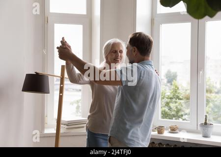 Happy mature loving couple holding hands dance in living room Stock Photo