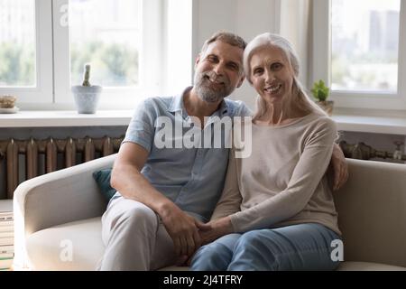 Happy loving mature couple pose seated on sofa at home Stock Photo