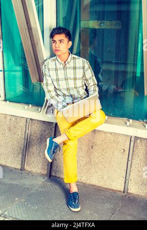 man working outside dressing in a white yellow patterned shirt yellow pants blue sneakers a young handsome college student is sitting by metal st