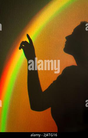 Shadow of woman. Rainbow reflection of sunbeam on wall. Hand touches rainbow beam. Concept of dreams and hopes. Stock Photo