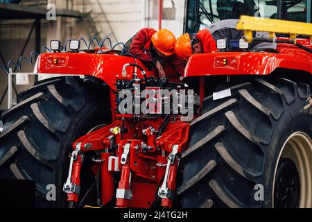Industrial workers assembles agricultural tractor in workshop. Stock Photo