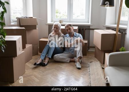 Tired elderly couple sit on floor near boxes with belongings Stock Photo