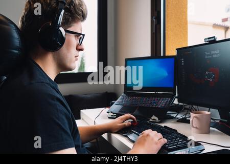 young blond man listening to music through headphones on computer sitting at desk. Stock Photo