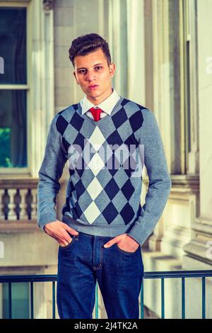 Portrait of College Student. Dressing in a black, white, gray patterned sweater, jeans, hands in pockets, a young handsome businessman is standing by Stock Photo
