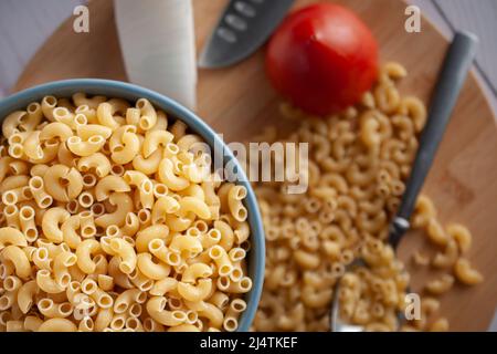 Raw or uncooked Elbow Pasta in a blue bowl and on a wooden chopping board with a spoon on the side top view Stock Photo