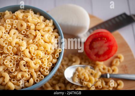 Raw or uncooked Elbow Pasta in a blue bowl and on a wooden chopping board with a spoon on the side top view Stock Photo