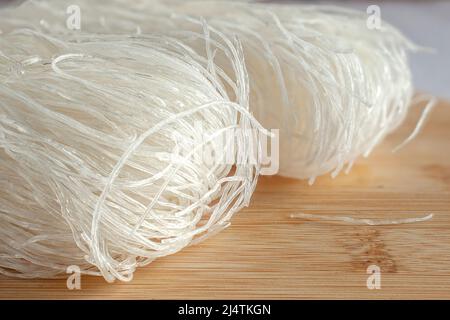 Raw or uncooked dry rice noodles on a wooden cutting or chopping board. Macro Photography horizontal side view Stock Photo