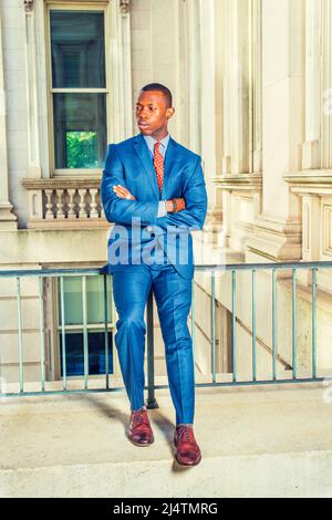 Man Waiting for You. Dressing formally in blue suit, patterned undershirt, tie, leather shoes, short haircut, crossing arms, a young black businessman Stock Photo
