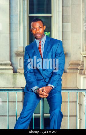 Portrait of Black Businessman. Dressing formally in blue suit, patterned undershirt, tie, short haircut, holding hands, a young handsome black guy is Stock Photo