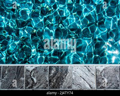 Grey tiles with marble pattern, empty space on the poolside edge floor for objects or summer products placed near the blue water surface of the swimmi Stock Photo